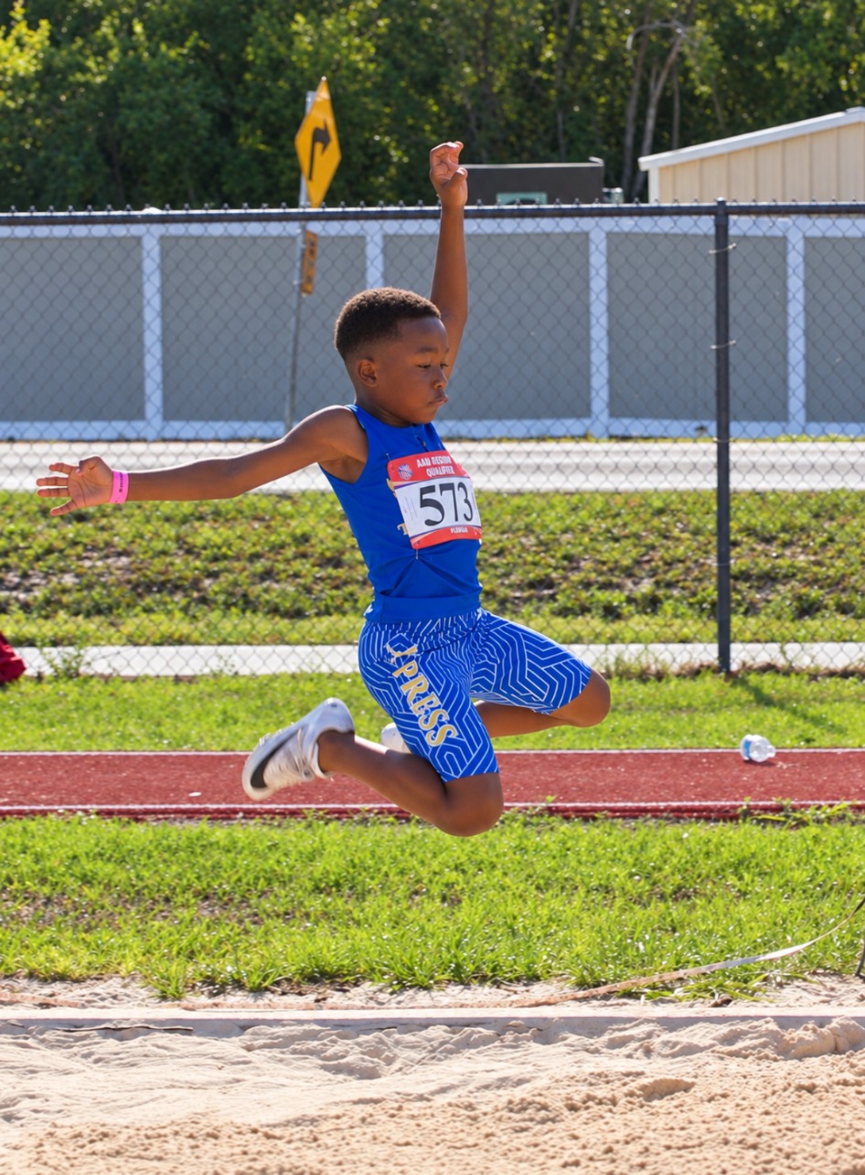 Young Tampa Xpress athlete jumping into the sand during a long jump competition